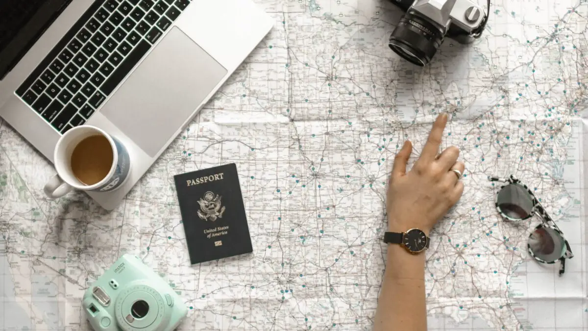 Adventure idioms - a map with a laptop, passport, camera and a person pointing at the map